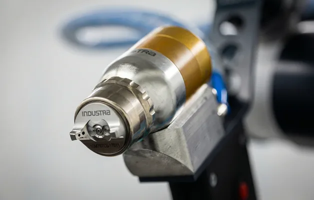 Detailaufnahme einer luftzerstäubenden Lackierpistole mit INDUSTRA Gravur, Fokus auf Luftkappe